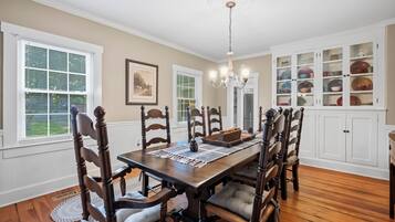 A dining room with a wooden table, chairs, a chandelier, and a cabinet with dishes.