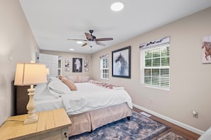 A bedroom with a bed, a nightstand, a ceiling fan, and horse-themed artwork on the walls.