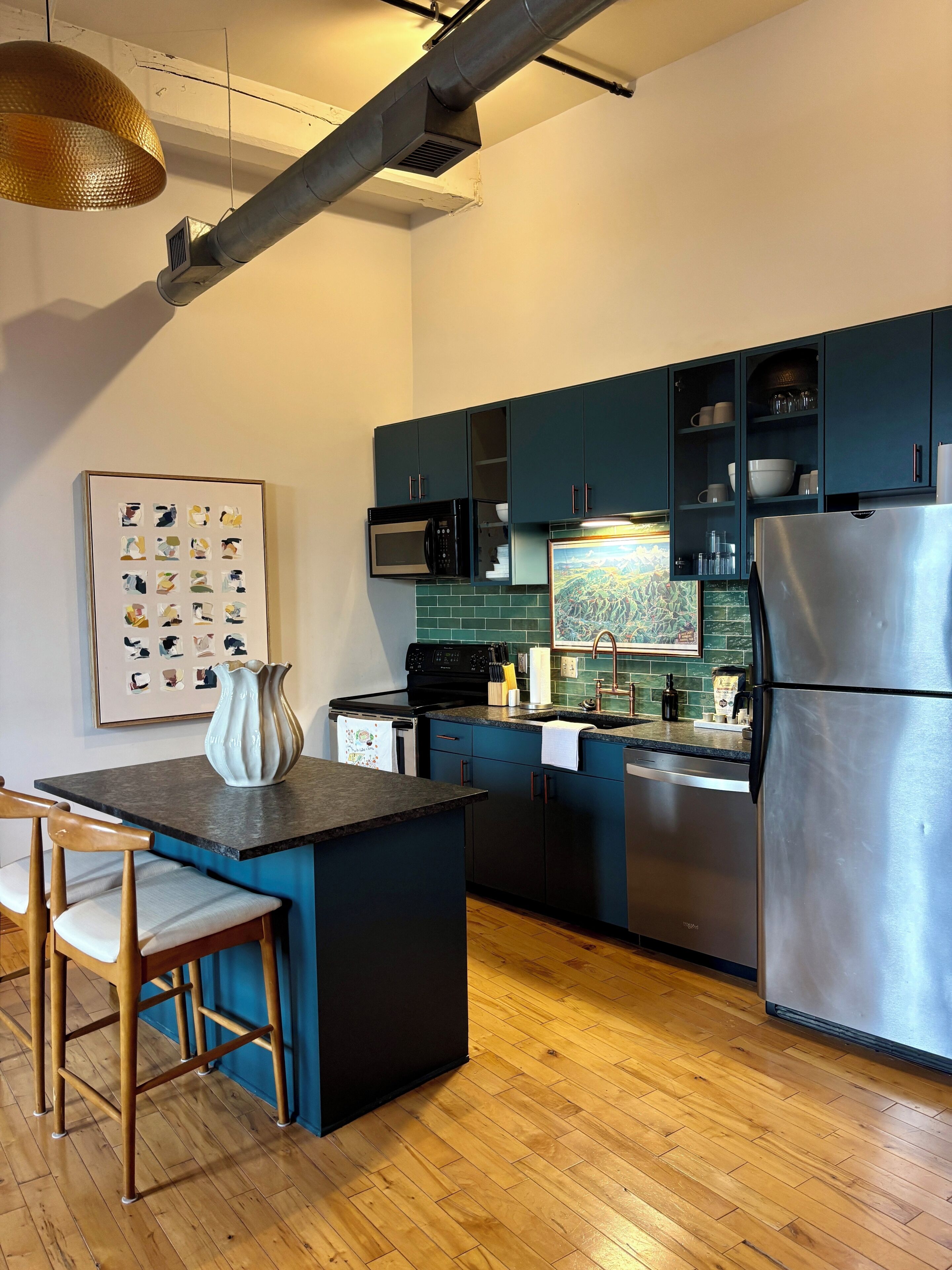 Une cuisine moderne dotée d’un îlot central, d’appareils électroménagers en acier inoxydable et de meubles de couleur turquoise.