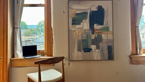 A room with a wooden floor, a desk with a laptop, a chair, a framed abstract painting, and a window with curtains. - Old City 2BR Condo close to Downtown and UTK: excellent walkablity (Knoxville)