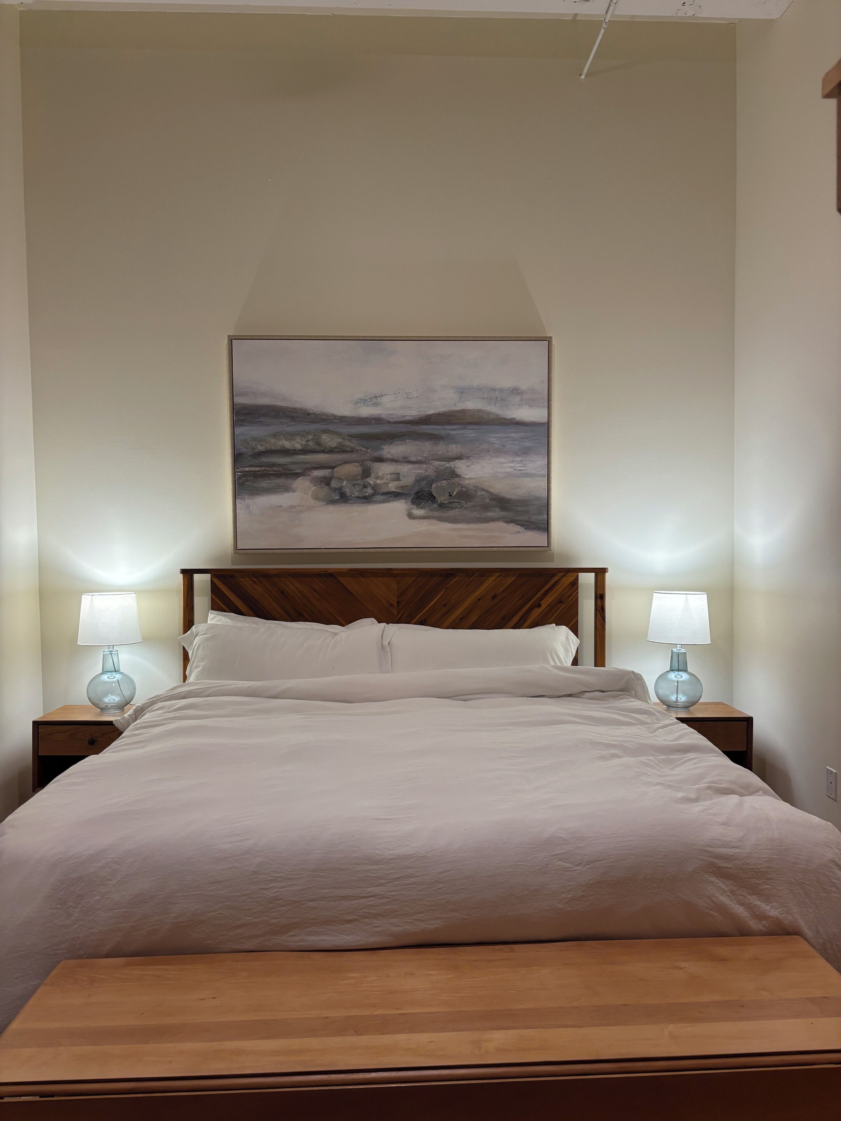 Une chambre à coucher avec un lit, deux lampes de chevet, une tête de lit en bois et un tableau au mur.