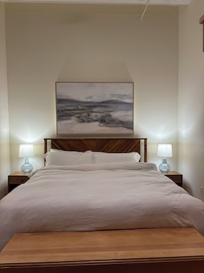 Ein Schlafzimmer mit einem Bett, zwei Nachttischlampen, einem hölzernen Kopfteil und einem Bild an der Wand.