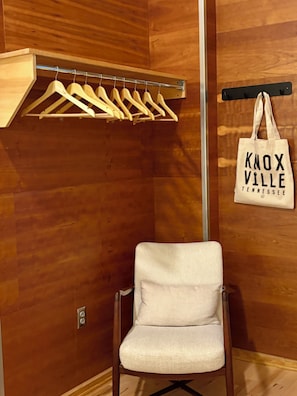 Ein Zimmer mit einer Holzwand, einem weißen Stuhl, Holzkleiderbügeln auf einem Metallgestell und einer Tasche mit dem Aufdruck 'Knoxville Tennessee'.