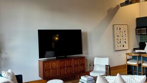 A living room with a television, wooden cabinet, blue sofa, brown leather sofa, and a ceiling fan. - Old City 2BR Condo close to Downtown and UTK: excellent walkablity (Knoxville)