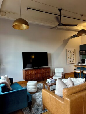 Ein Wohnzimmer mit Fernseher, Holzschrank, blauem Sofa, braunem Ledersofa und Deckenventilator.