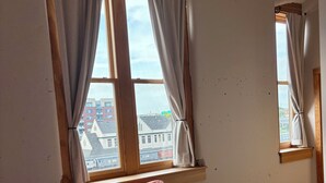 A room with a red sofa, two windows with curtains, a wooden floor, and a view of buildings outside. - Old City 2BR Condo close to Downtown and UTK: excellent walkablity (Knoxville)