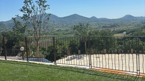 A grassy area with a metal fence, a tree, and a clear view of distant hills. - Flumendosa Apartment, Stunning View of the Euganean Hills (Veneto)
