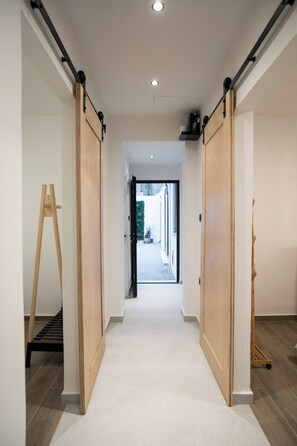 A hallway with a wooden floor, a sliding door on the left, and a door on the right. - Athelio Boutique Home • Private Garden • Outdoor Bar • Near Metro (Pireas)
