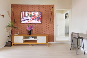 A living room with a brick wall, a flat-screen TV, a wooden console table, a potted plant, and a wicker chair. - Cabana Mata Verde Pool/Lake - Tomorrowland (Itu)