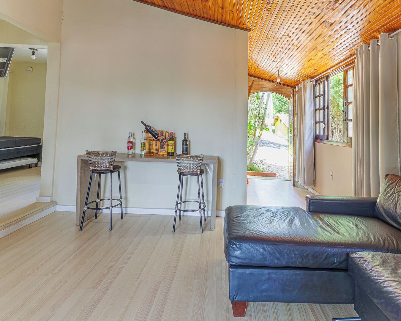 Ein Zimmer mit Holzbalkendecke, einer Bar mit Hockern, einer Couch und Blick durch ein Fenster.