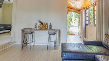 A room with a wooden ceiling, a bar area with stools, a sofa, and a view through a window.