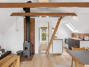A modern loft with a wood-burning stove, a kitchen with a skylight, and a staircase leading to a balcony. - 5 Star Holiday Home in Dannemare (Dannemare)