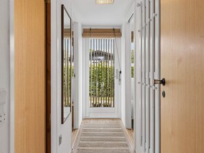 A hallway with a wooden door, a mirror, and a view of a garden through a window with vertical blinds. - 5 Star Holiday Home in Dannemare (Dannemare)