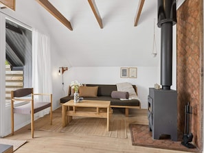 A cozy living room with a sofa, a wooden coffee table, a chair, a fireplace, and a staircase leading to an upper level. - 5 Star Holiday Home in Dannemare (Dannemare)