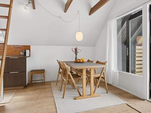 A dining area with a wooden table and chairs, a small side table, and a window with blinds. - 5 Star Holiday Home in Dannemare (Dannemare)