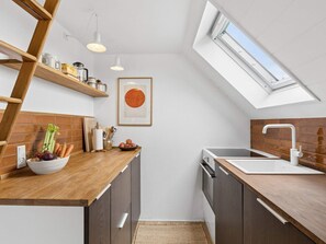 Eine kleine Küche mit Oberlicht, Holzregalen und einer weißen Spritzschutzwand.