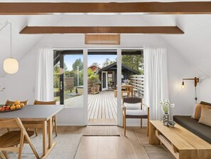 A modern interior with a wooden dining table, chairs, a sofa, and a bench. There is a sliding glass door leading to an outdoor deck.
