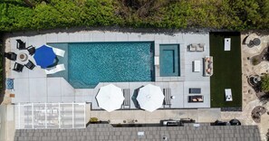 Eine Vogelperspektive eines Poolbereichs mit rechteckigem Pool, Liegestühlen, Sonnenschirmen und einem kleinen Garten.