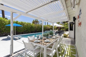 Une terrasse extérieure avec une piscine, des meubles blancs et des parasols.