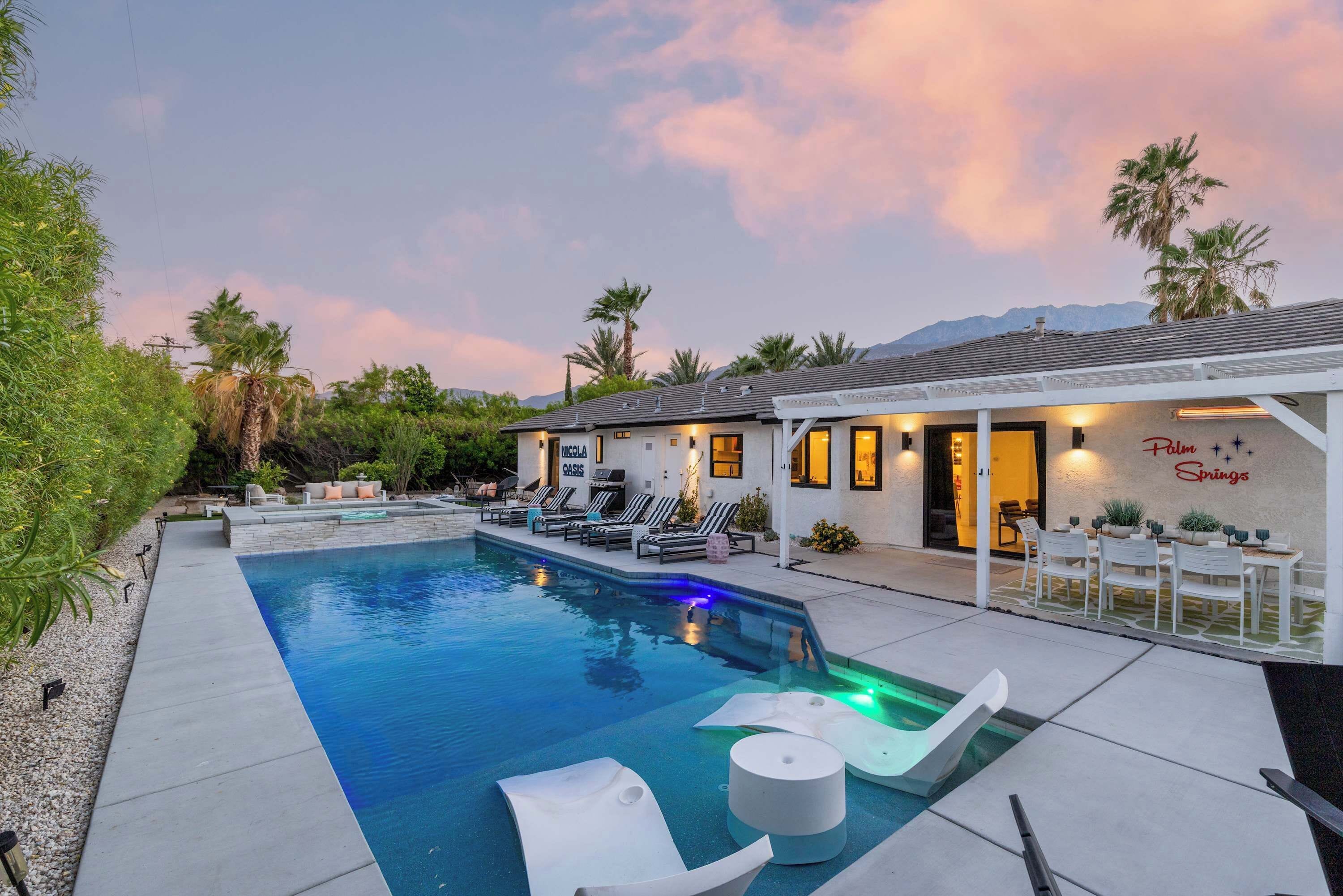 A modern outdoor pool area with lounge chairs and a barbecue, surrounded by greenery and a mountain backdrop.