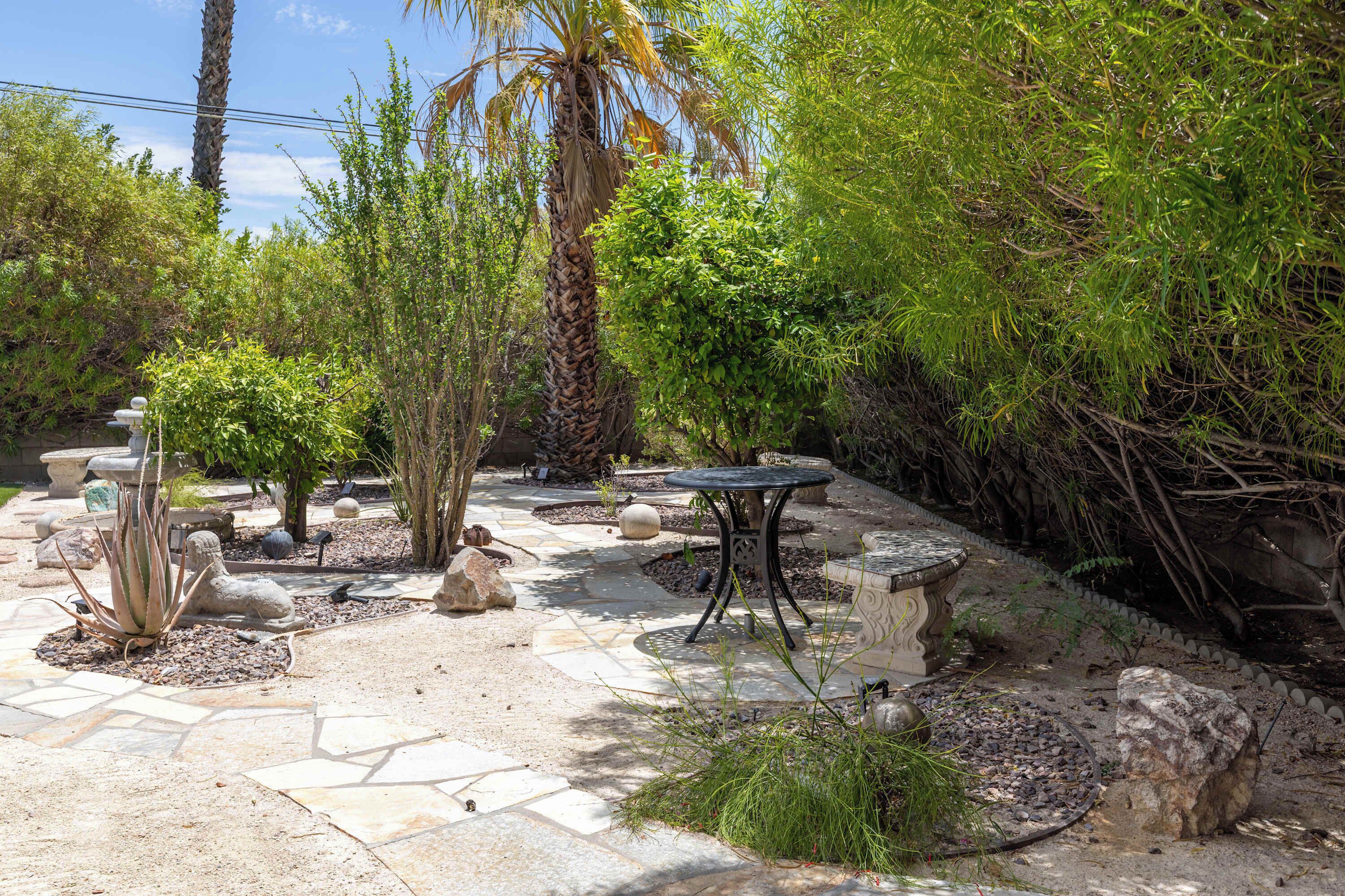 A garden with a variety of plants, a stone pathway, and a metal table.