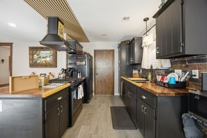 A modern kitchen with dark cabinetry, a central island, and a built-in stove. - Cozy Getaway, an ultimate Tulsa suburb retreat and a backyard oasis. (Tulsa)