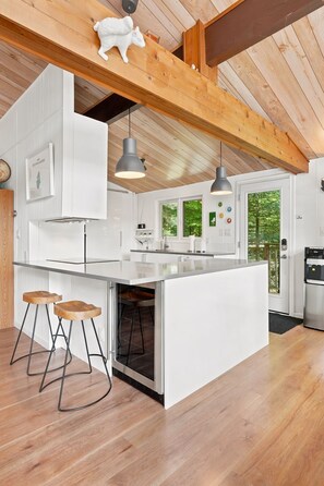 Een moderne keuken met een groot eiland, houten balken, hanglampen en uitzicht op de omgeving.