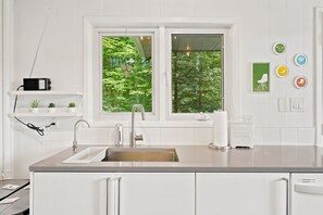 A modern kitchen with a double sink, white cabinetry, and a window with a view of greenery. - Muskoka River Cottage - Kayaks, Firepit, BBQ, Wifi (Bracebridge)