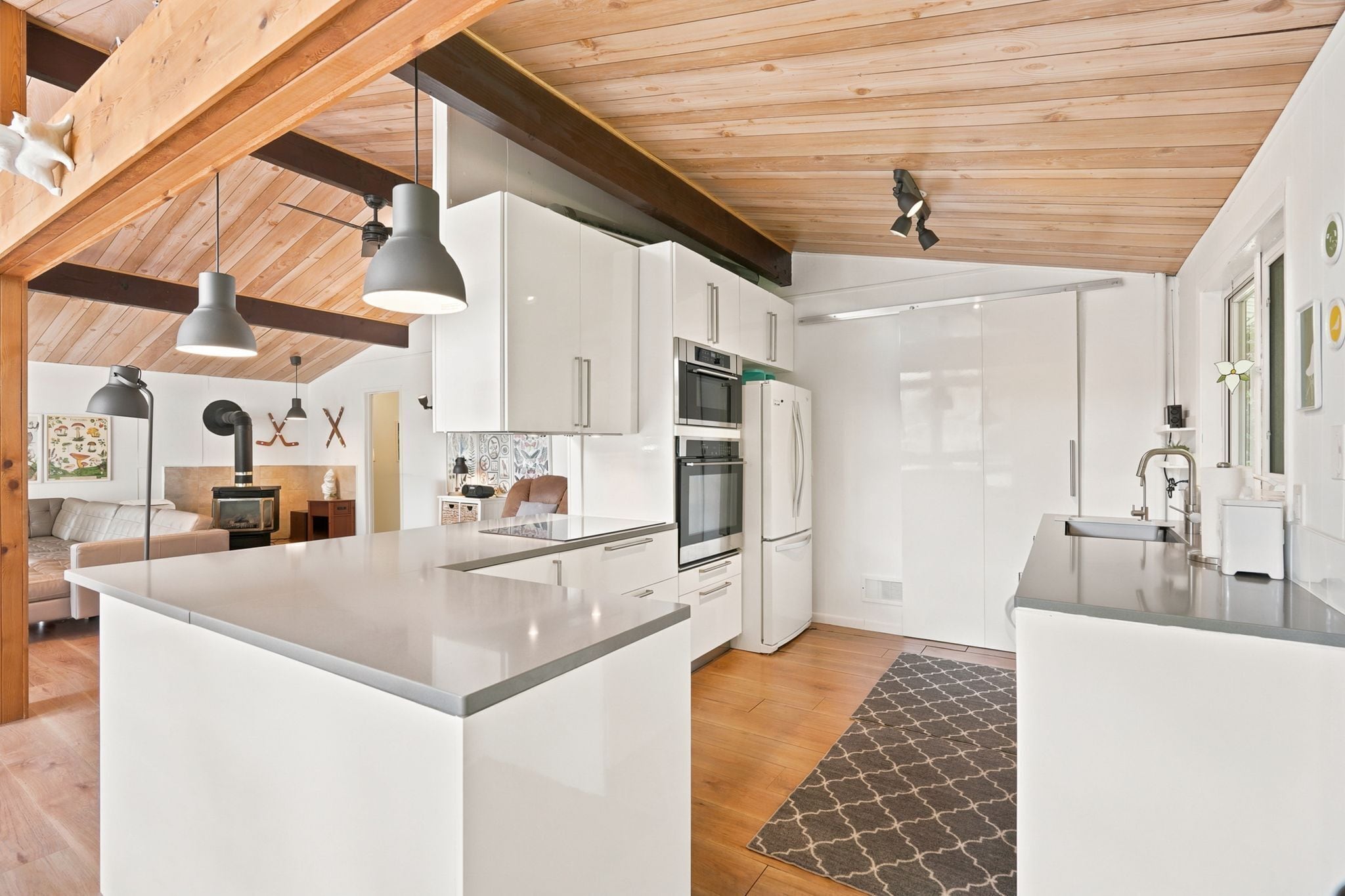 Une cuisine moderne avec des meubles blancs, des appareils en acier inoxydable et un plafond en bois.