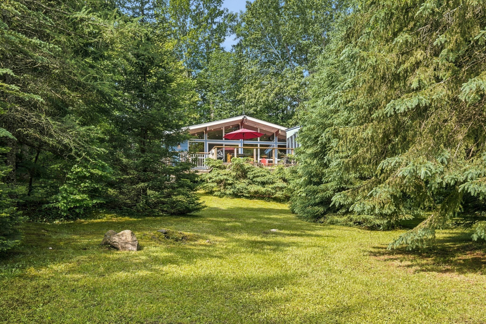 A house surrounded by dense forest, with a well-maintained lawn and a large rock in the foreground.
