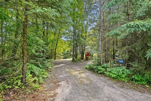 A forested area with a gravel path leading to a red structure, possibly a cabin or shelter, and a blue sign with the number 1245. - Muskoka River Cottage - Kayaks, Firepit, BBQ, Wifi (Bracebridge)