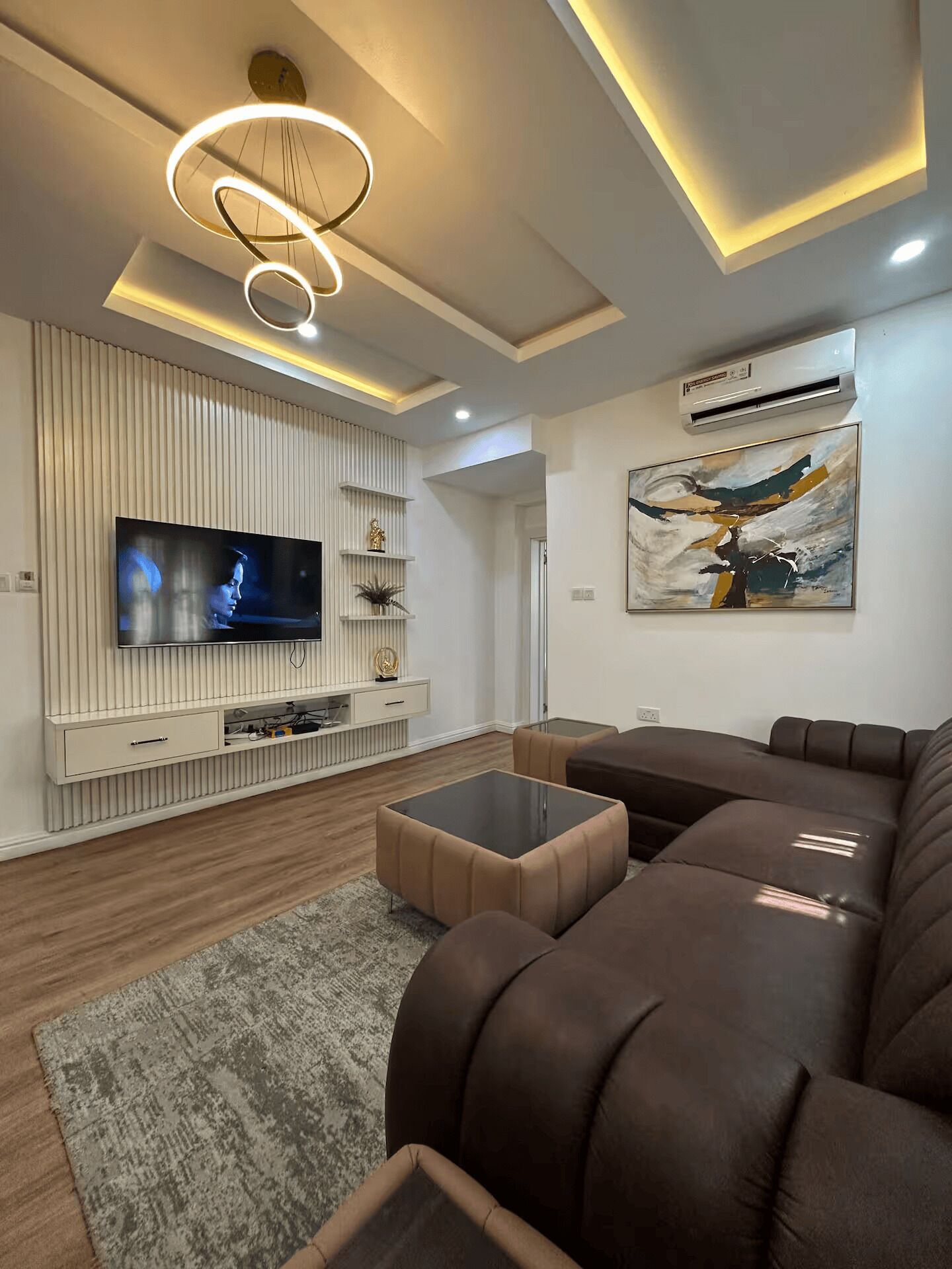 A modern living room with a flat-screen TV, a sectional sofa, a glass coffee table, and a contemporary art piece on the wall.