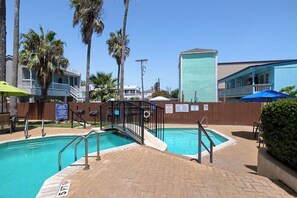 A swimming pool with a wooden deck, surrounded by palm trees and a fence. - Seas the day! Just a 5 minute walk to the beach! 2bd 2 bath sleeps 8 (South Padre Island)