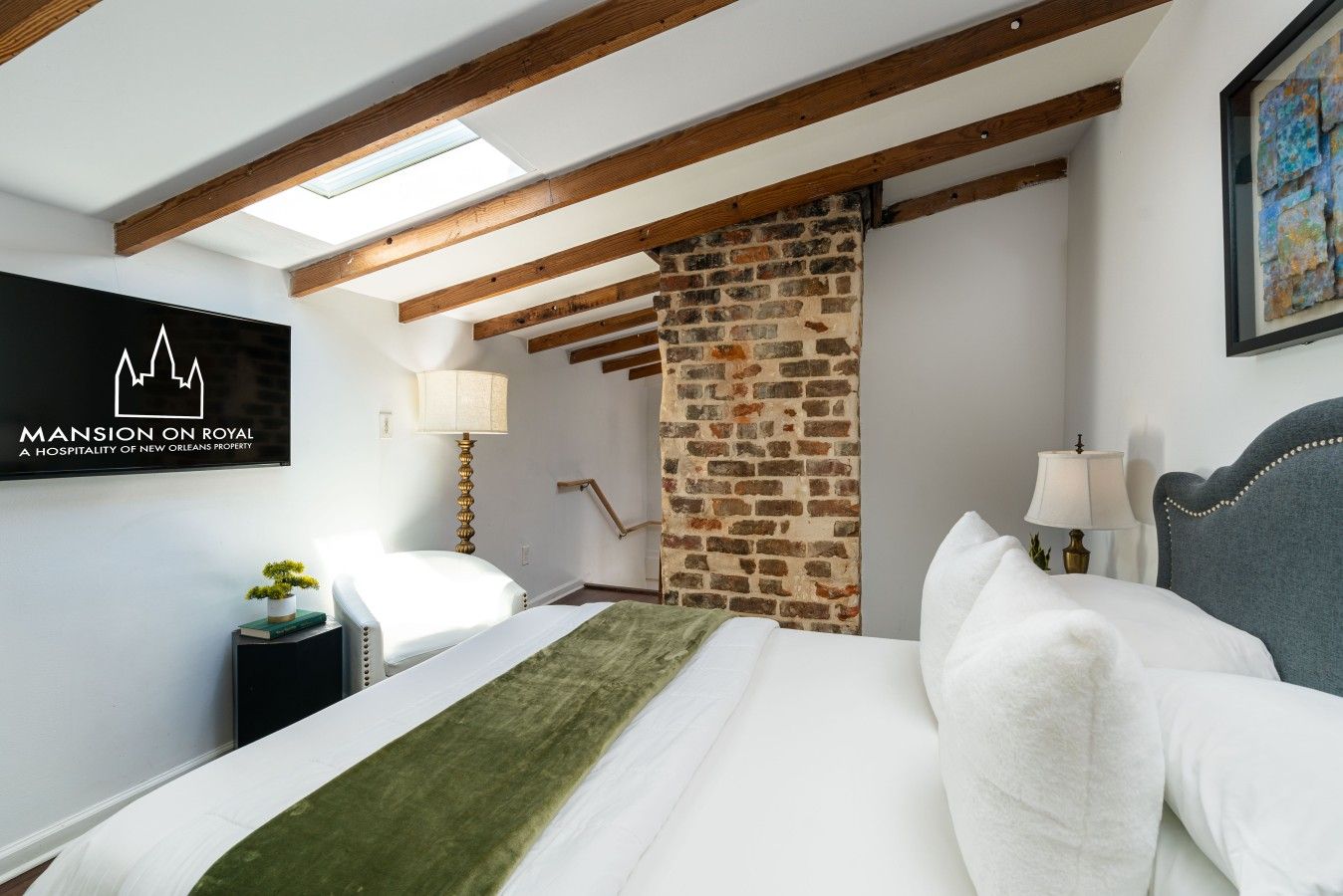 A hotel room with a bed, a nightstand, a lamp, a wall-mounted TV, and a stone wall.