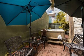 An outdoor patio with a hot tub, metal chairs, and umbrellas.