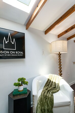 A room with a white leather chair, a lamp, a small potted plant, and a framed sign on the wall.