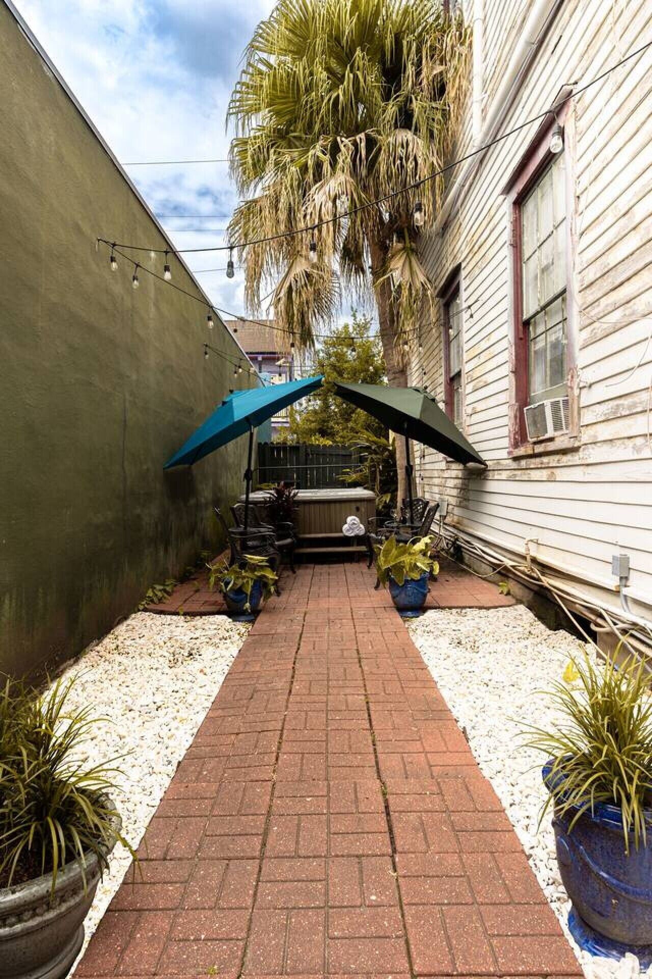 A paved patio with a covered seating area, potted plants, and a building with siding.