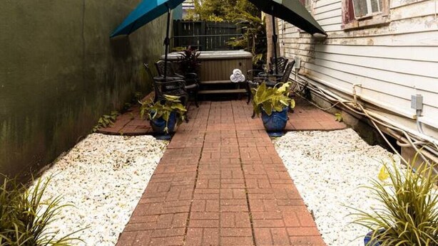 Um pátio pavimentado com área de estar coberta, plantas em vasos e um edifício com revestimento.