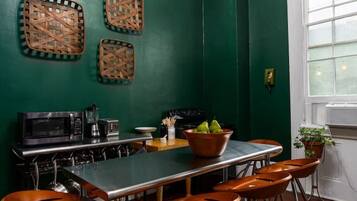 A kitchen with a dark green wall, a white ceiling, and a chandelier. There are three woven baskets on the wall, a microwave, a coffee maker, and a stove.