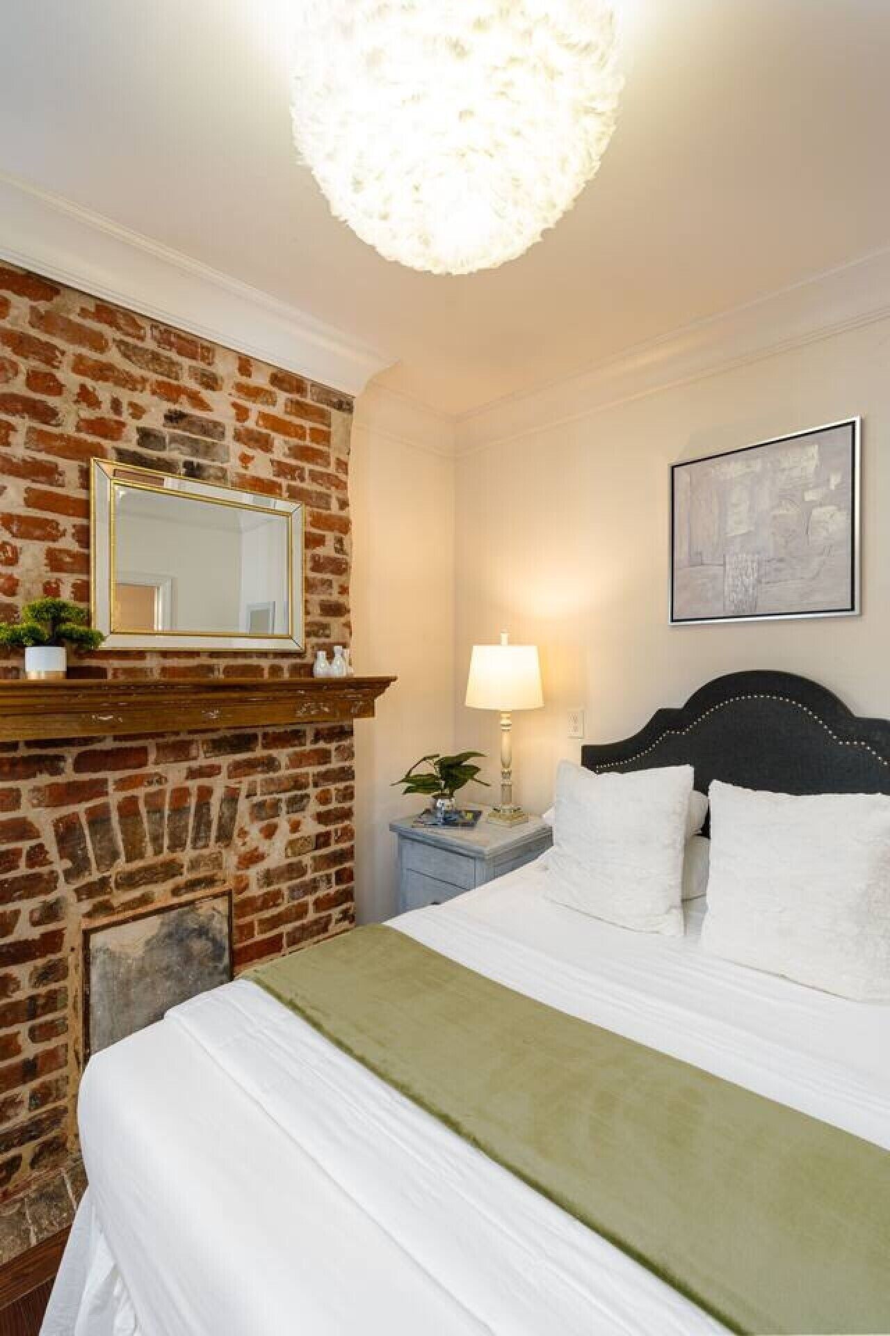 A hotel room with a brick wall, a bed with white bedding, a nightstand with a lamp, and a framed picture on the wall.