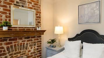 A hotel room with a brick wall, a bed with white bedding, a nightstand with a lamp, and a framed picture on the wall.