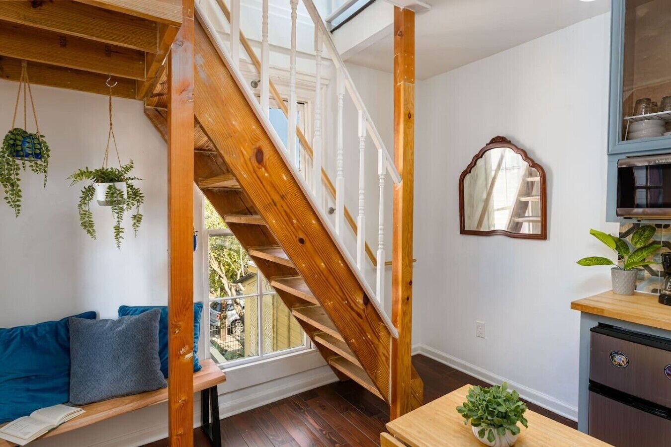 Ein Zimmer mit einer Holztreppe, einem blauen Sofa, einem Esstisch mit einer Pflanze und einer Küchenzeile mit Schränken.