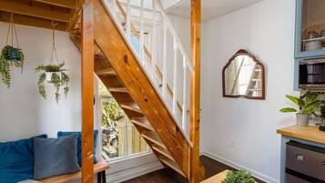 A room with a wooden staircase, a blue sofa, a dining table with a plant, and a kitchen area with cabinets.