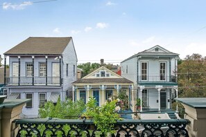 Una hilera de casas de tres pisos con balcones, una casa central con techo a dos aguas y una cerca en primer plano.