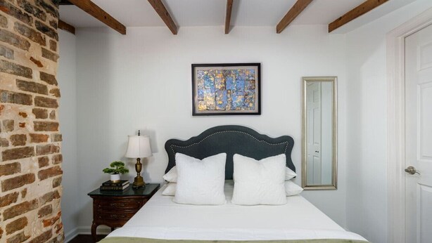 A bedroom with a bed, a nightstand, a lamp, a framed artwork, and a mirror. - Historic Carriage House | Walk to Quarter & Music (New Orleans)