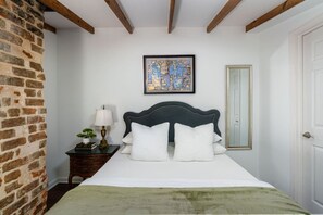 A bedroom with a bed, a nightstand, a lamp, a framed artwork, and a mirror.