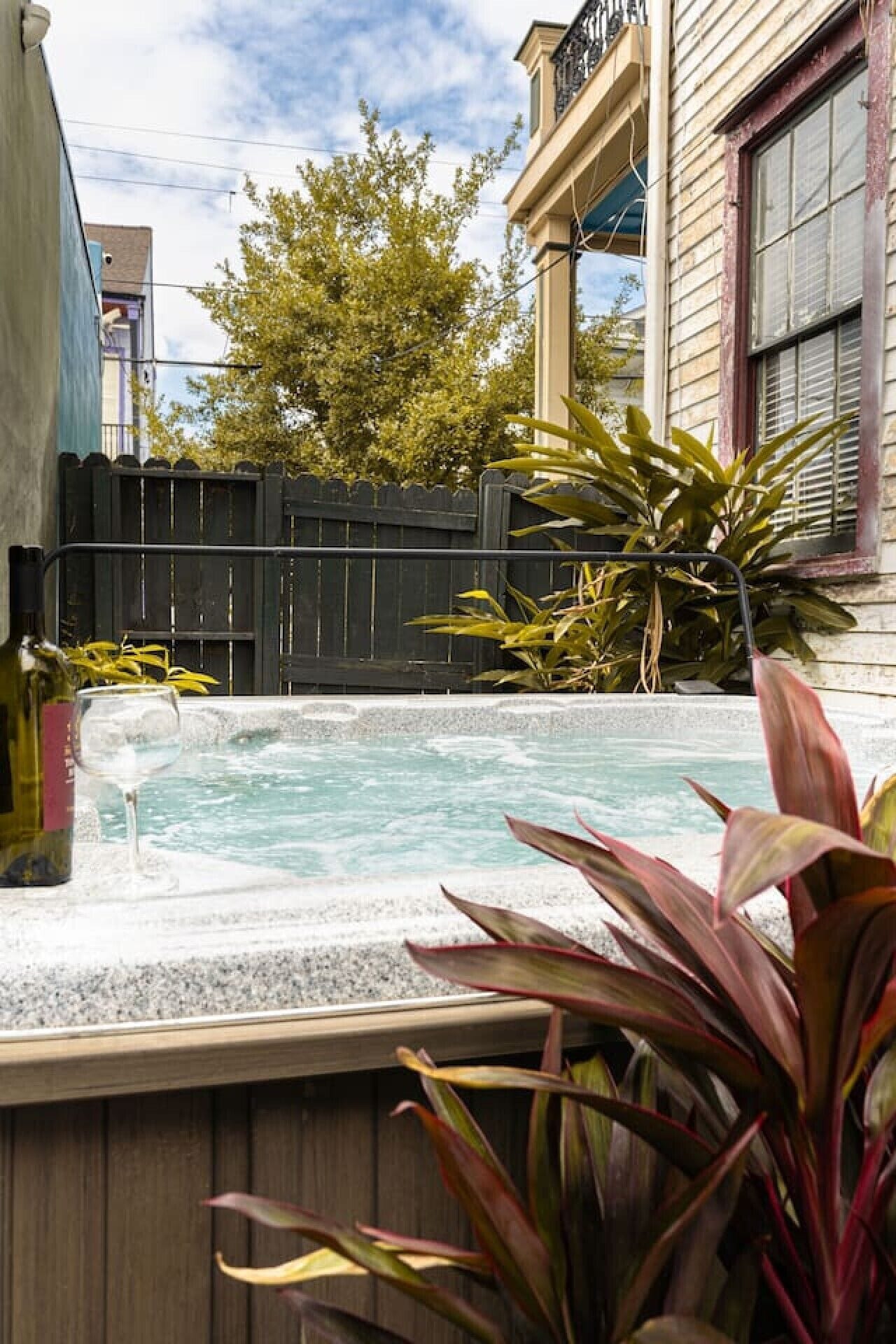 Ein Whirlpool mit Holzterrasse, umgeben von Pflanzen und einem Zaun.