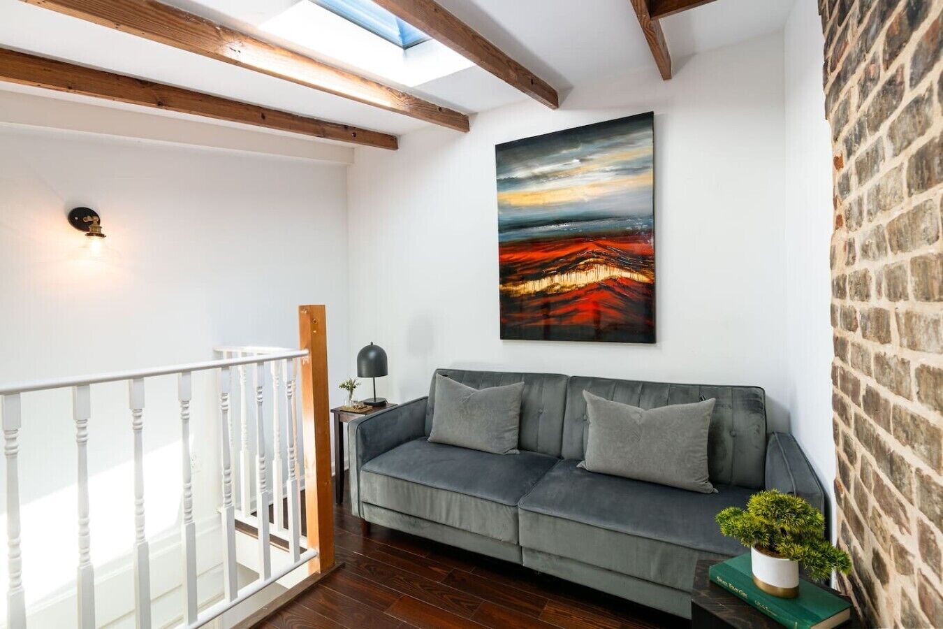 Uma sala de estar moderna com um sofá cinzento, uma pintura e uma parede de tijolos.
