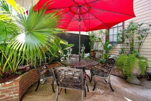 En terrasse med et rundt bord, stole, en rød parasol og forskellige planter.