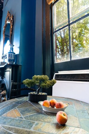 A room with a stone-tiled table, a bonsai tree, and a bowl of fruit.